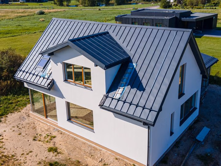 Aerial view of a two-story white house topped with a dark gray standing seam metal roof.