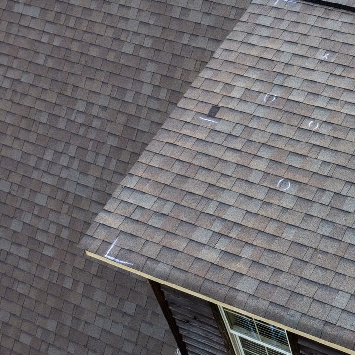 Aerial view of a brown asphalt shingle roof marked with chalk circles highlighting hail‑damaged areas, labeled “REPAIRS.”
