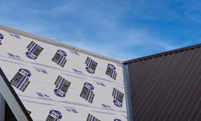 Metal Roof underlayment installation in progress showing white synthetic underlayment with blue logos partially covered by dark metal roofing panels against a blue sky with white clouds